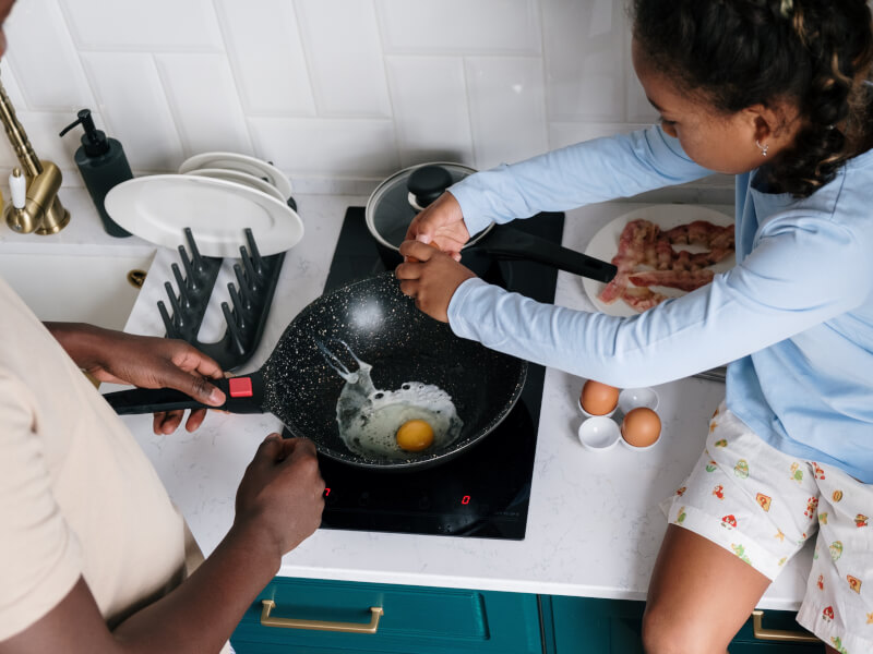 Young girl learning to fry an egg with her father